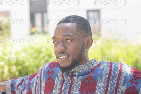 Young black man sitting on bench with African poncho