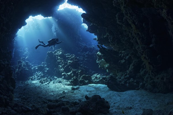 Sunbeams shining through reef top in cave in coral reef with diver