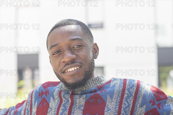 Young black man sitting on bench with African poncho