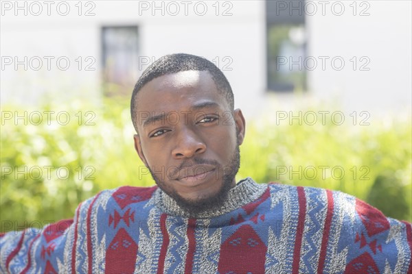 Young black man sitting on bench with African poncho