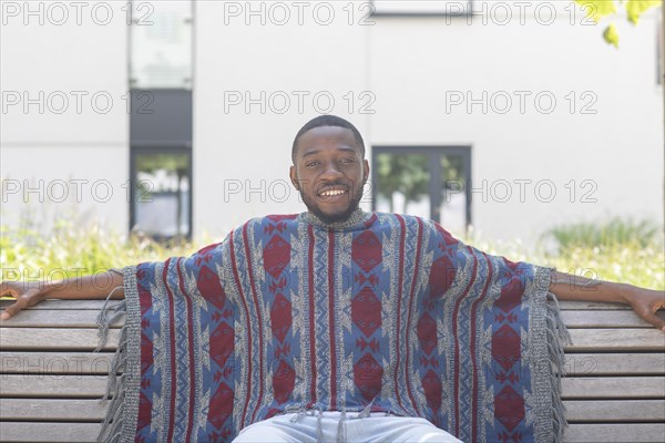 Young black man sitting on bench with African poncho