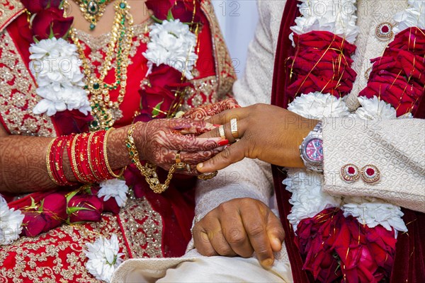 Bride with bridal jewelry and henna decoration on her hand attaches ring to the groom's finger at traditional religious ceremony at a Hindu wedding