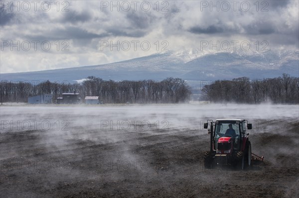 Tractor seeding a field while it is vaporating from the warm ground