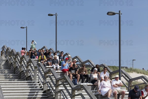 Holidaymakers sitting on wooden steps one behind the other