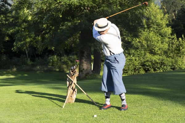 Older man in straw hat and knickerbockers playing hickory golf on a golf course