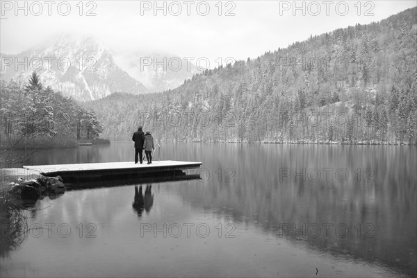 Lake with reflection and footbridge with two people in winter black and white