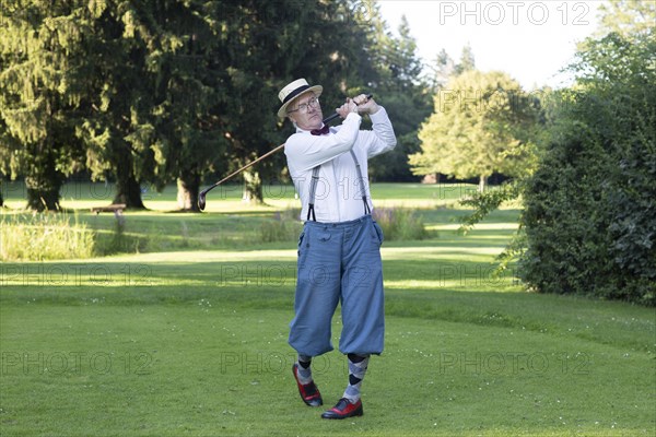 Older man in straw hat and knickerbockers playing hickory golf on a golf course