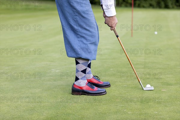 Older man in straw hat and knickerbockers playing hickory golf on a golf course