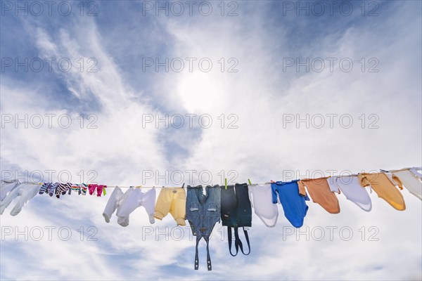 A lot of small baby clothes hanging against blue cloudy sky