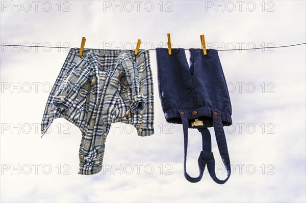 Elegant baby trousers and shirt pinned with wooden pegs against cloudy sky