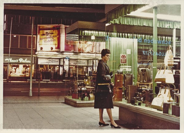 Stuttgart at night in 1963: A young woman with a coat and handbag looks at the display of handbags and suitcases in a leather goods shop
