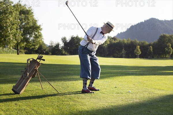 Older man in straw hat and knickerbockers playing hickory golf on a golf course