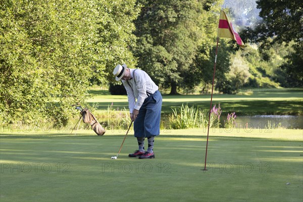 Older man in straw hat and knickerbockers playing hickory golf on a golf course