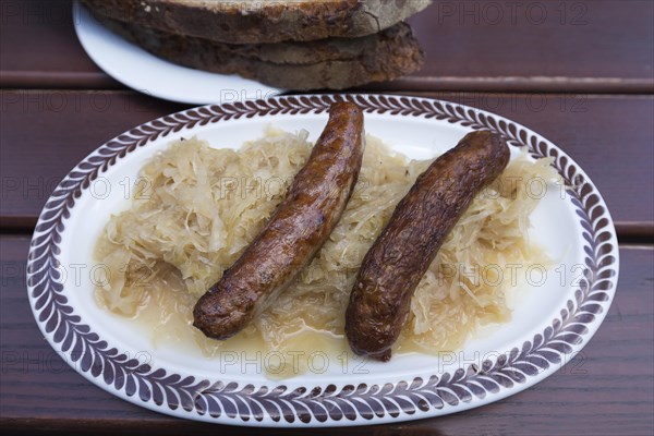 Two Nuremberg bratwursts with sauerkraut and bread on an oval plate in a garden restaurant