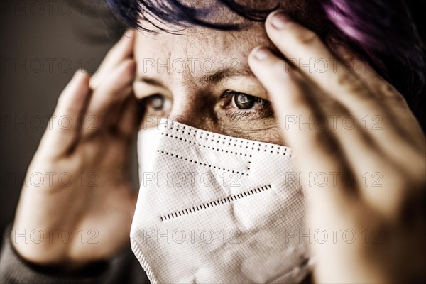 Woman with FFP2 medical mask looks thoughtful and holds hands to her head