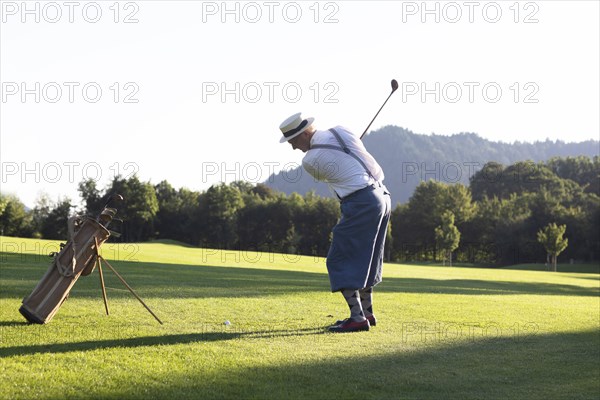 Older man in straw hat and knickerbockers playing hickory golf on a golf course