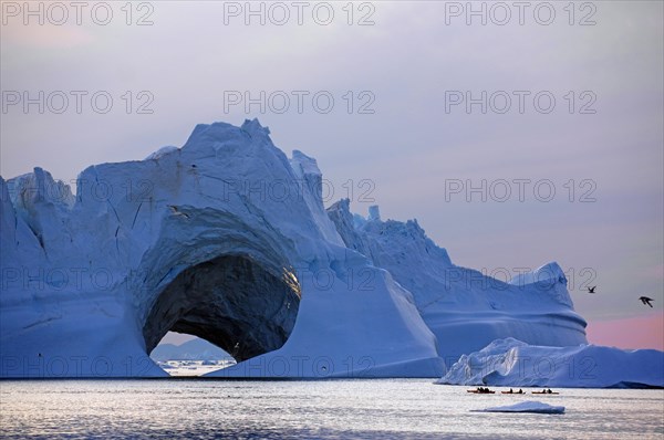Kayaks in front of huge iceberg with cave