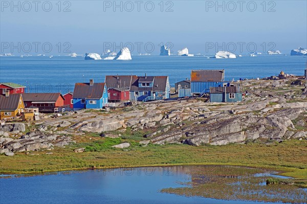Wooden houses and rocks in front of a bay filled with icebergs