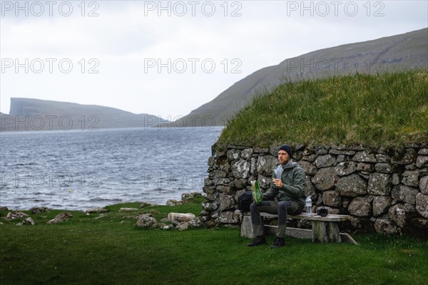 Hiker eating biscuits on a bench in front of a stone hut