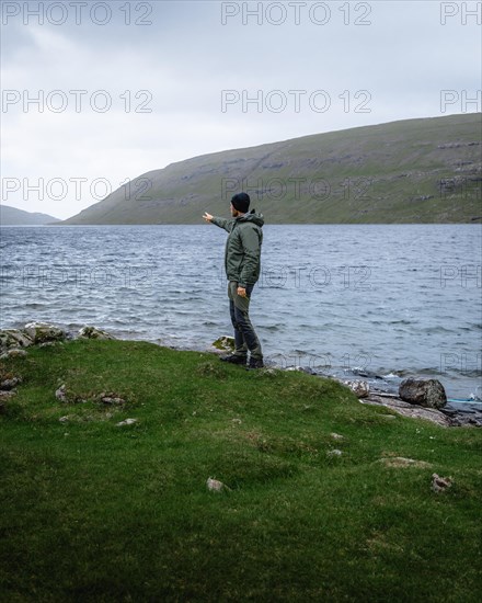 Hiker standing on the shore of Lake Leitisvatn pointing into the distance