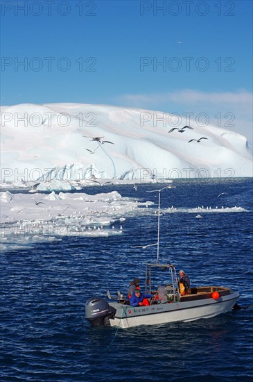 Small fishing boat in front of huge icebergs and drift ice