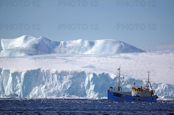 Small fishing boat in front of huge icebergs and drift ice