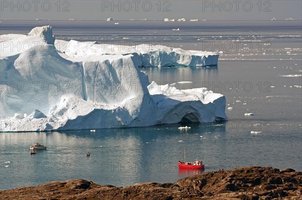 Red fishing boat in a bay with huge icebergs