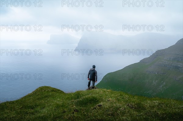 Person standing on the mountain looking at the village of Mikladalur