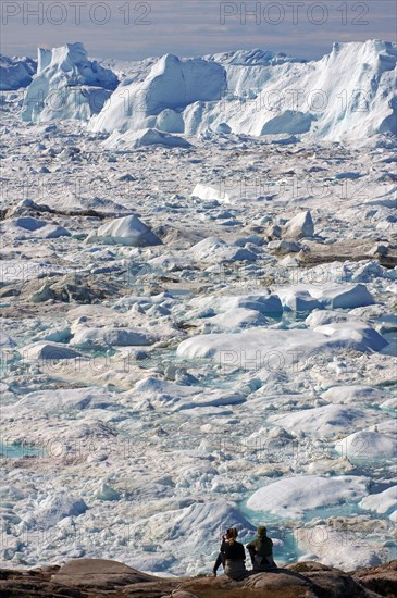 People sitting in front of fjord covered with ice and icebergs