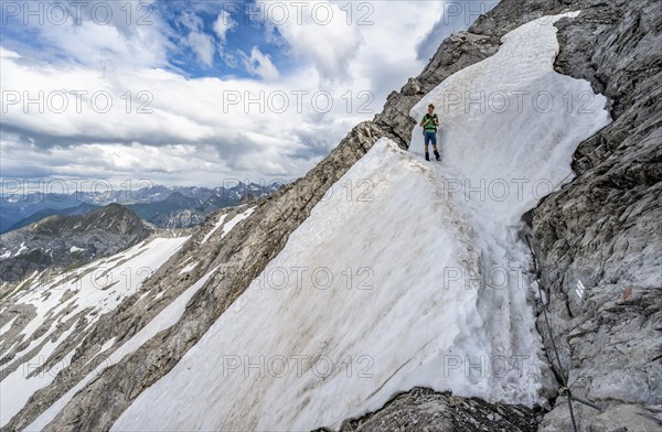 Hiker descending over remnants of snow in rocky terrain