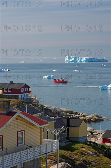 Wooden houses in front of a bay with fishing boat and icebergs