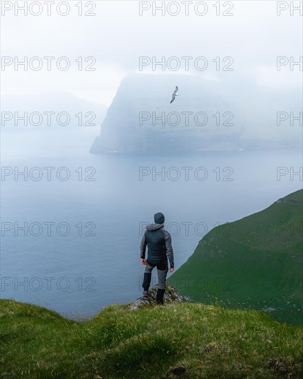 Person standing on the mountain looking at the village of Mikladalur