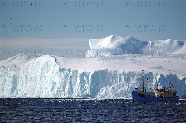 Small fishing boat in front of huge icebergs and drift ice