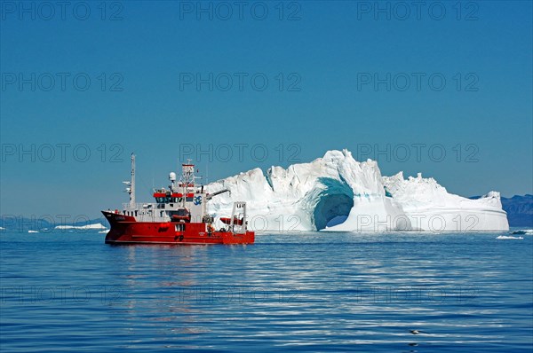 Red research vessel in front of iceberg with LOch
