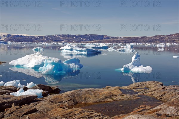 Barren rocks in front of icebergs reflected in the water of a fjord