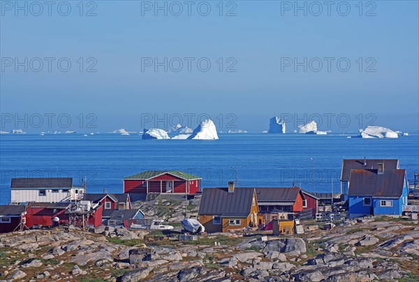 Wooden houses and rocks in front of a bay filled with icebergs