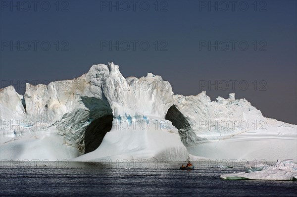 View of small fishing boat in front of huge iceberg with 2 holes