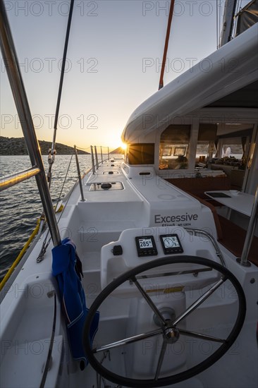 Steering wheel in the cockpit on the deck of a sailing catamaran at sunset