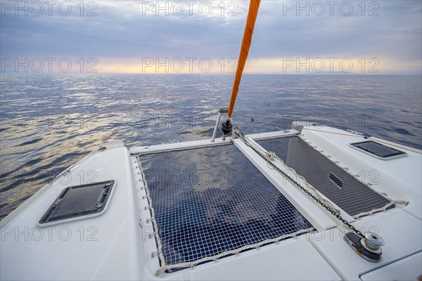 Recessed headsail and deck with net of a sailing catamaran in evening light