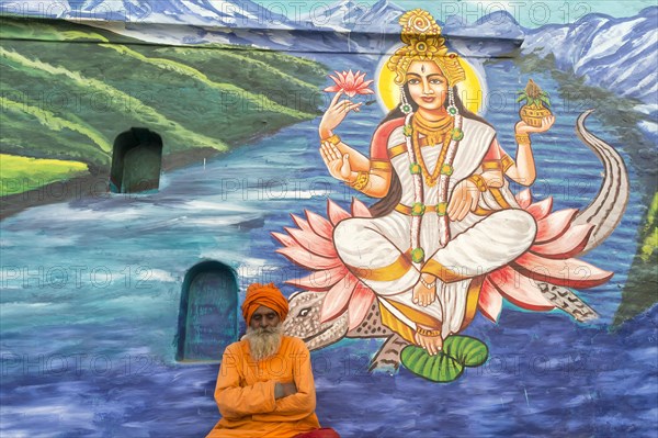 Sadhu in saffron robes in front of an image of a deity