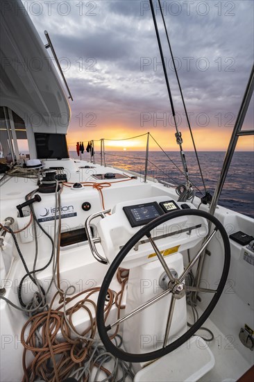 Steering wheel in the cockpit on the deck of a sailing catamaran at sunset