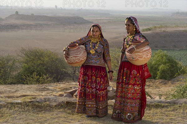 Two Ahir woman in traditional colorful dress carrying water in a clay jug