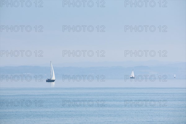 Three sailing boats on shimmering blue Lake Constance in sunny weather and blue skies in summer