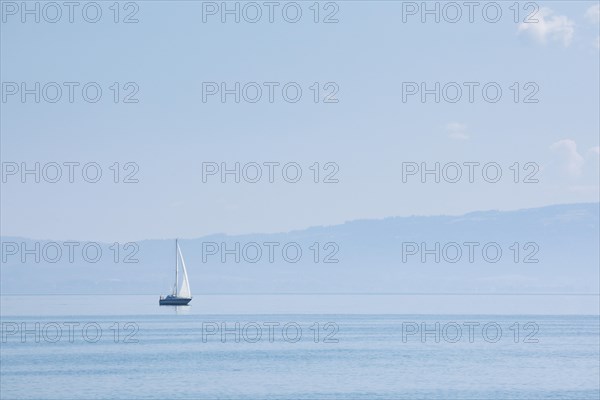 Sailing boat on shimmering blue Lake Constance in sunny weather and blue sky in summer