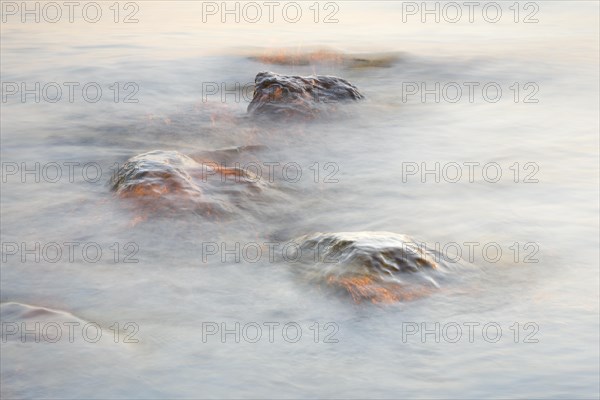 Light play and stones in the water at sunrise photographed with slow shutter speed