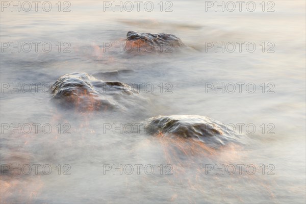 Light play and stones in the water at sunrise photographed with slow shutter speed