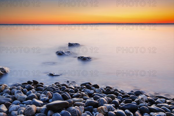 View over Lake Constance at sunrise with stones in the foreground and photographed with slow shutter speed