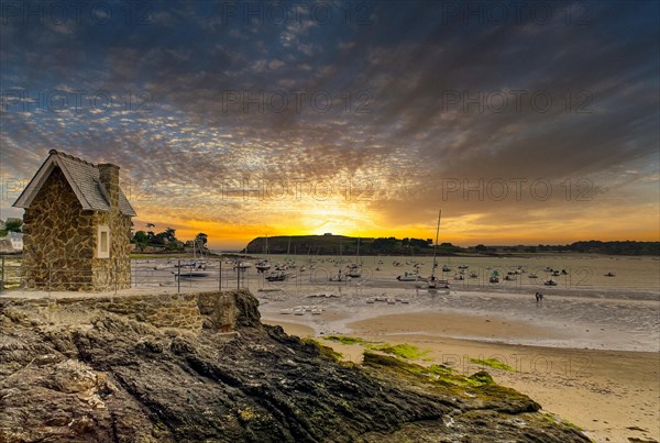 Small harbour at low tide with fishing boats and a small stone house at a dramatic sunrise