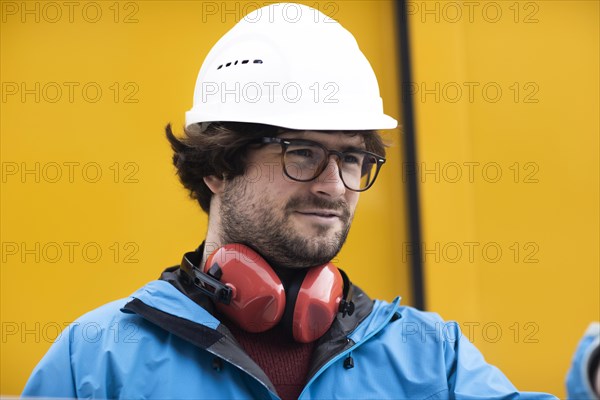 Young engineer with helmet and hearing protection at a work site outside