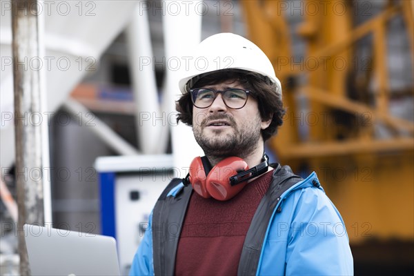 Young engineer wearing a helmet and hearing protection at a work site outside on a construction site